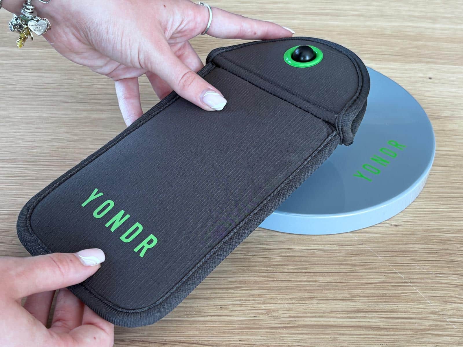 dark grey and green Yondr Phone Pouch held by two hands above a grey unlocking base